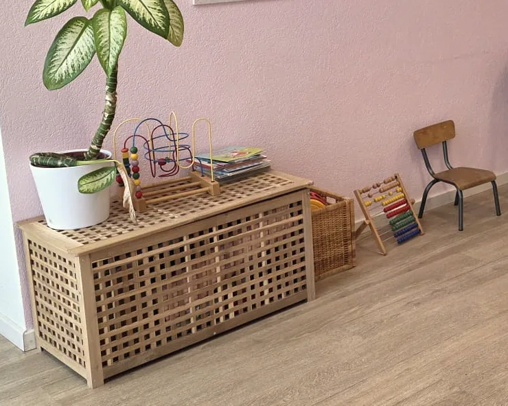 Coin des enfants dans la salle d’attente : coffre en bois, jeux, boulier et petite chaise contre un mur rose